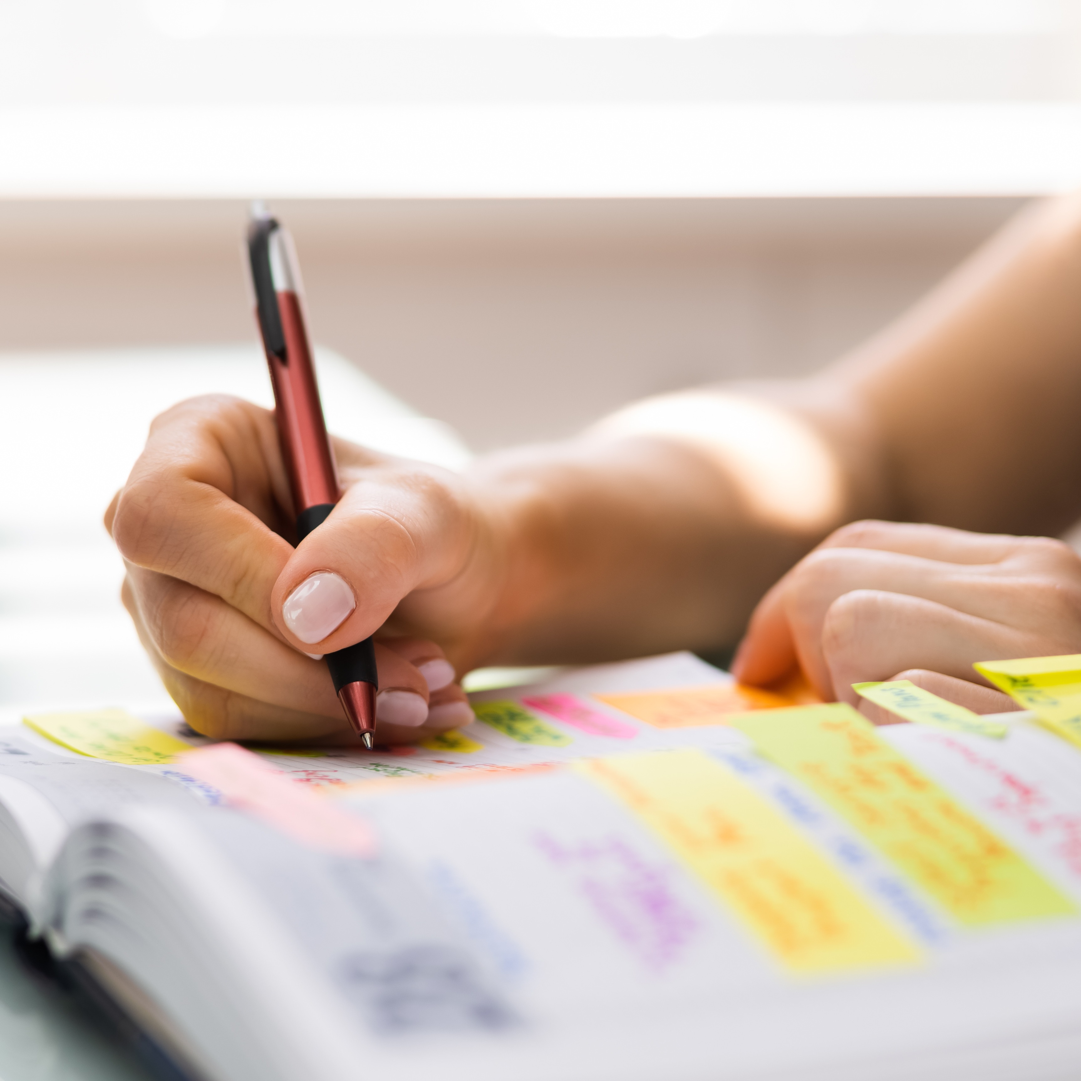 A book with words highlighted in yellow, pink, and purple is being written in with a brown pen.  